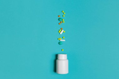 Virüs enfeksiyonlarına karşı bağışıklık kazanarak. Farklı renkte vitaminler, haplar ve mavi kapsüllerle dolu beyaz bir şişe. Coronavirus, evde kalma kavramı