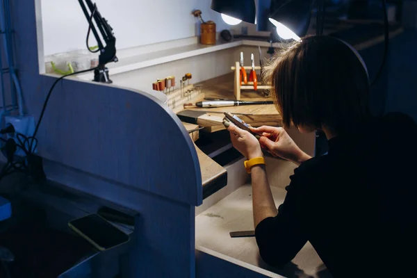 The girl works on a jewelry in the workshop. Working tools on the table. Handicraft people art concept. She makes silver ring.