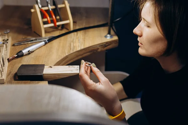 The girl works on a jewelry in the workshop. Working tools on the table. Handicraft people art concept. She makes silver ring.