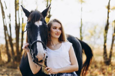 Çiftlikte atın yanında şık, sarışın bir kadın. Gülümseyen kız ata sarılıyor. İnsan ve hayvan ilişkileri kavramı