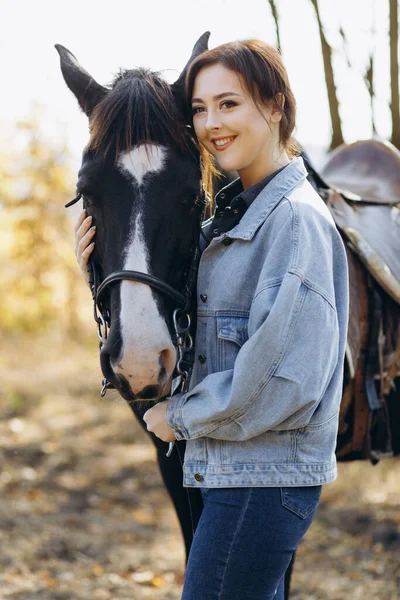 牧場の馬の近くの美しいスタイリッシュなブルネットの女性 笑顔の少女は馬を抱いている 人間と動物の関係の概念 — ストック写真