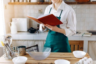 Mutfakta durup yemek tarifi kitabı arayan, ne pişireceğini seçmeye çalışan bir kadın resmi. Ev konseptinde aşçılık, yaşam tarzı.