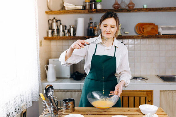 Молодая счастливая девушка стоит на кухне за столом и будет печь торт. Она блогер по еде. Здоровый образ жизни. Готовить дома. Кетогенная диета и меню
