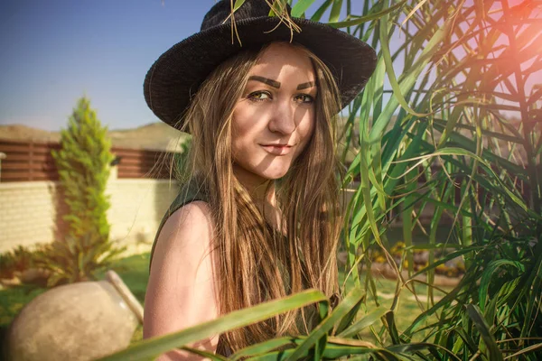 Menina bonita nova em um chapéu preto e longo dressin o g ensolarado — Fotografia de Stock