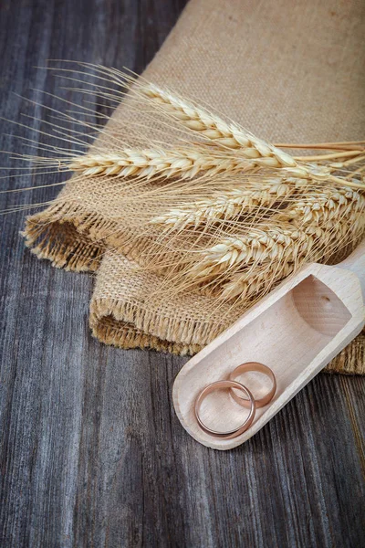 Trouwringen in een houten lepel en oren van tarwe — Stockfoto