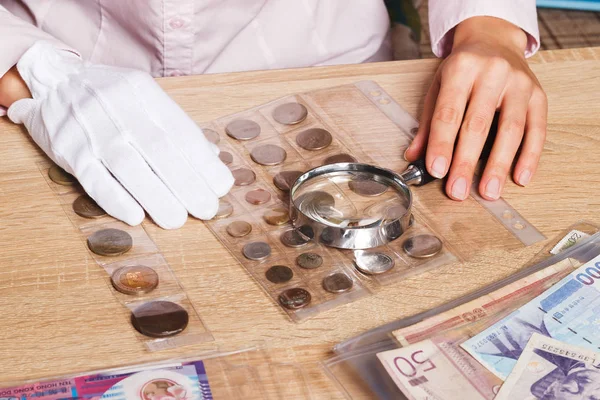 Woman looks at the coins through a magnifying glass — Stock Photo, Image