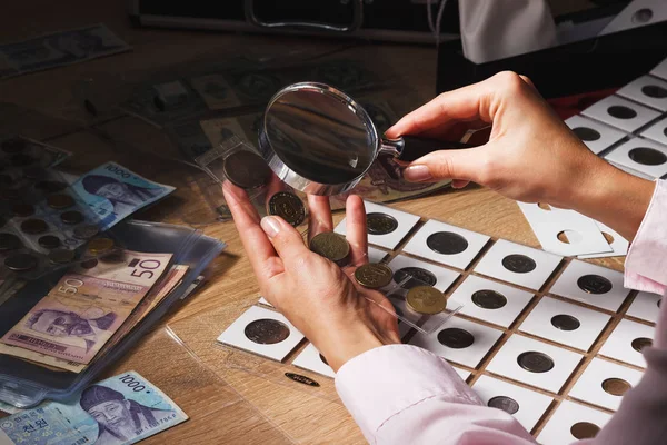 Mujer mira la moneda a través de una lupa —  Fotos de Stock