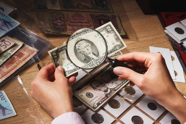 Woman looks at the Dollar bill through a magnifying glass — Stock Photo, Image