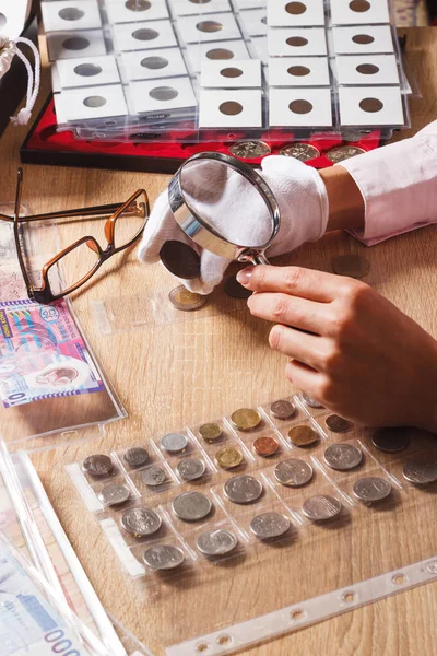 Mujer mira la moneda a través de una lupa —  Fotos de Stock