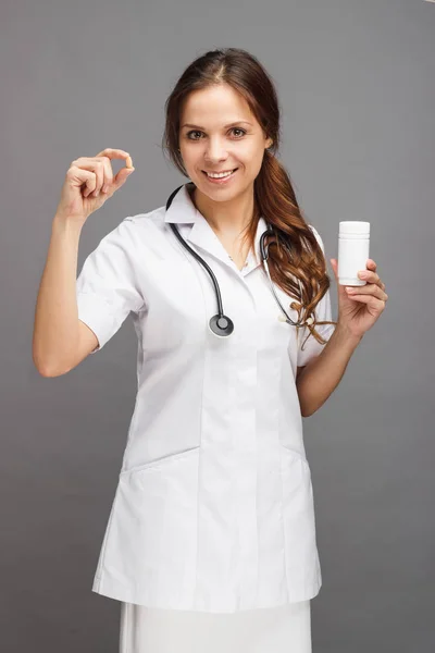 Mulher doutor no uniforme médico branco com um frasco de pílulas na mão — Fotografia de Stock