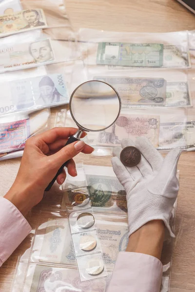 Hands with magnifying glass and an old collectible coin — Stock Photo, Image