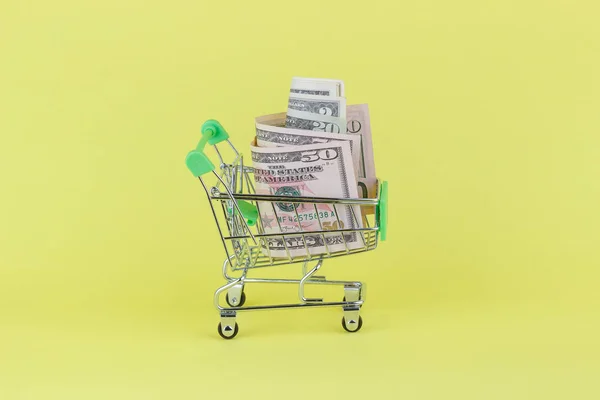 Amerikaanse dollars in de winkelstraat pushcart, gele achtergrond — Stockfoto