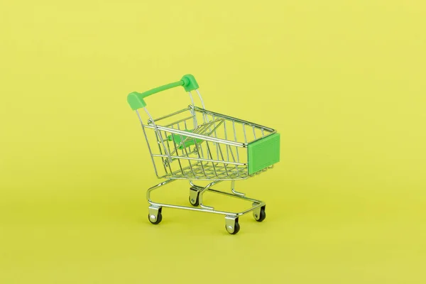 Lege miniatuur winkelen pushcart, gele achtergrond — Stockfoto