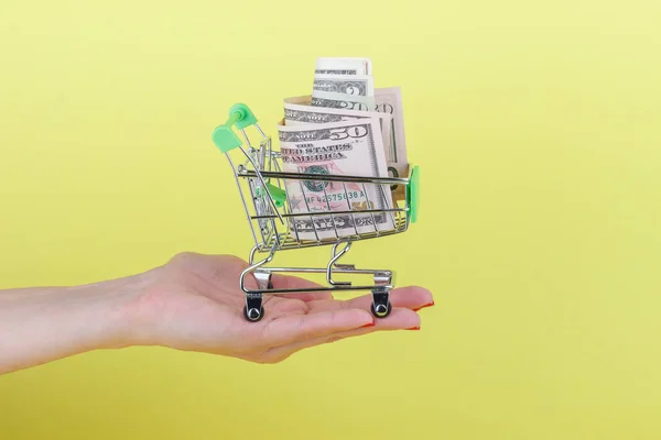 Amerikaanse dollars in de winkelstraat pushcart, gele achtergrond — Stockfoto