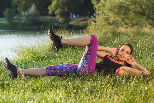 Sportieve vrouw aan de kust van de meren maakt sport oefeningen op de zonsondergang — Stockfoto