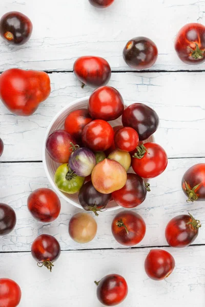 Verschillende tomaten in de kom op de witte houten achtergrond — Stockfoto