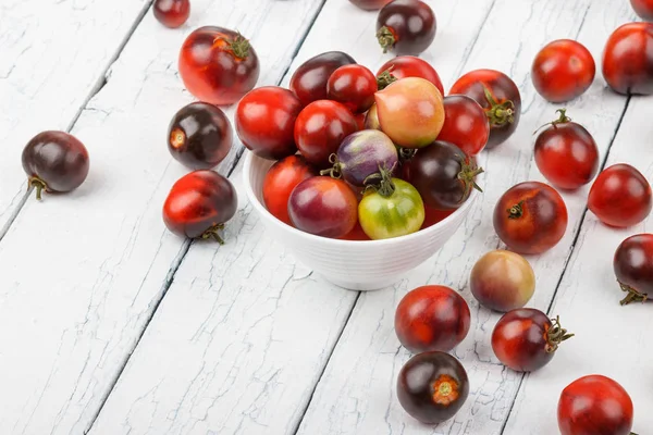 Verschiedene Tomaten in der Schüssel auf weißem Holzgrund — Stockfoto