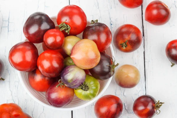 Verschillende tomaten in de kom op de witte houten achtergrond — Stockfoto