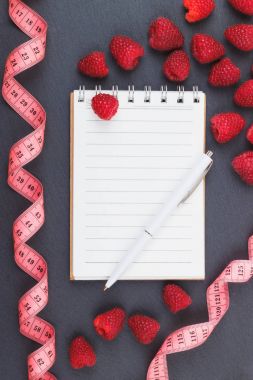 Kırmızı Ahududu, mezura, defter ve bir kalem siyah arduvaz taş zemin üzerine