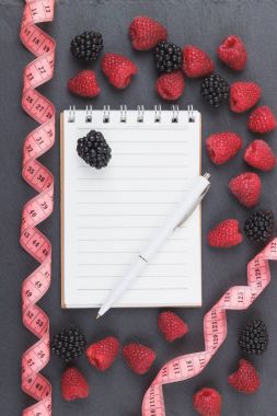 Kırmızı Ahududu, böğürtlen, mezura, defter ve bir kalem siyah arduvaz taş zemin üzerine