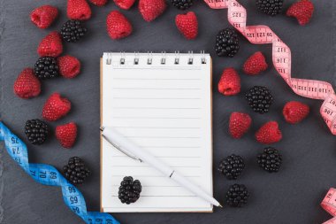 Kırmızı Ahududu, böğürtlen, mezura, defter ve bir kalem siyah arduvaz taş zemin üzerine