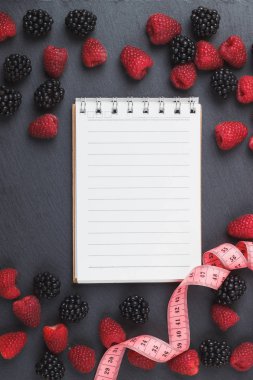 Kırmızı Ahududu, böğürtlen, mezura ve siyah arduvaz taş zemin üzerine defter