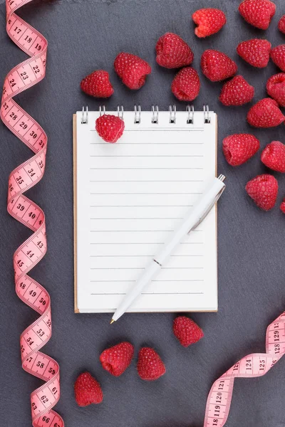 Kırmızı Ahududu, mezura, defter ve bir kalem siyah arduvaz taş zemin üzerine