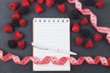 Kırmızı Ahududu, mezura, defter ve bir kalem siyah arduvaz taş zemin üzerine