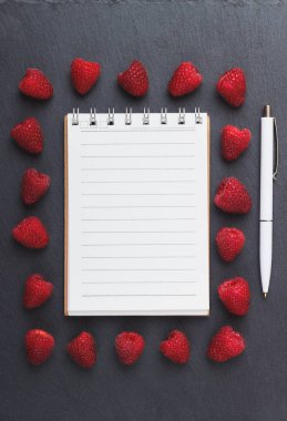 Kırmızı Ahududu, mezura, defter ve bir kalem siyah arduvaz taş zemin üzerine