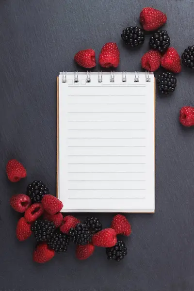 Kırmızı Ahududu, mezura, defter ve bir kalem siyah arduvaz taş zemin üzerine