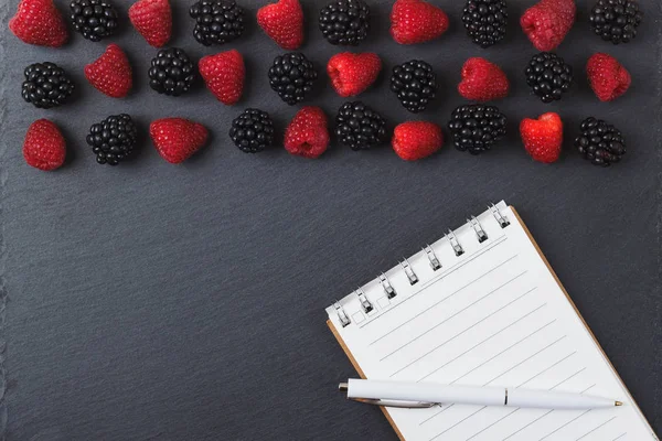 Kırmızı Ahududu, böğürtlen, defter ve bir kalem siyah arduvaz taş zemin üzerine