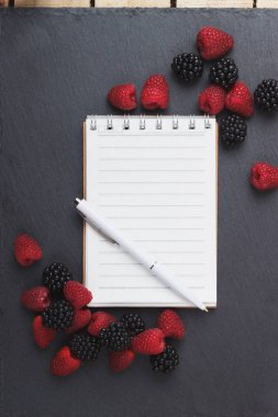 Kırmızı Ahududu, mezura, defter ve bir kalem siyah arduvaz taş zemin üzerine