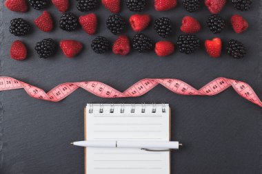 Kırmızı Ahududu, mezura, defter ve bir kalem siyah arduvaz taş zemin üzerine