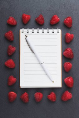 Kırmızı Ahududu, mezura, defter ve bir kalem siyah arduvaz taş zemin üzerine