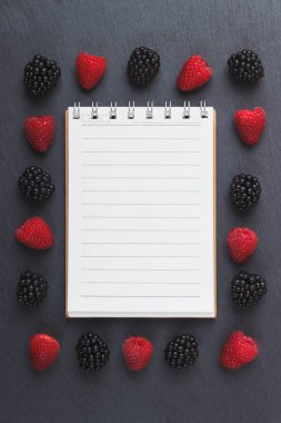 Kırmızı Ahududu, mezura, defter ve bir kalem siyah arduvaz taş zemin üzerine