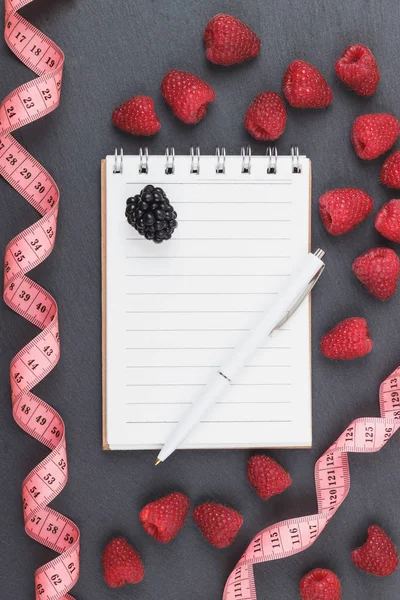 Kırmızı Ahududu, mezura, defter ve bir kalem siyah arduvaz taş zemin üzerine