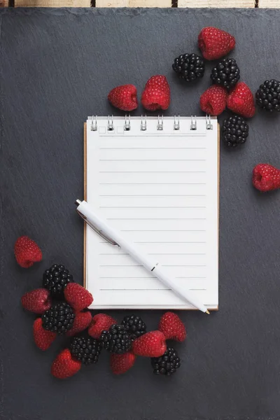 Kırmızı Ahududu, mezura, defter ve bir kalem siyah arduvaz taş zemin üzerine