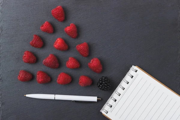 Kırmızı Ahududu, mezura, defter ve bir kalem siyah arduvaz taş zemin üzerine