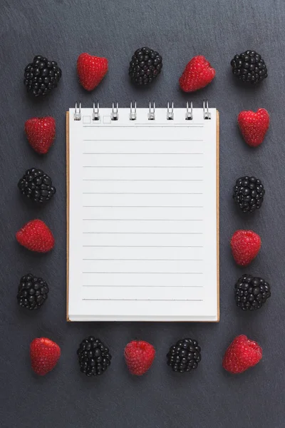 Kırmızı Ahududu, mezura, defter ve bir kalem siyah arduvaz taş zemin üzerine