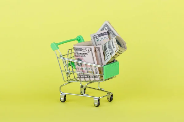 Amerikaanse dollars in de winkelstraat push kar, gele achtergrond — Stockfoto