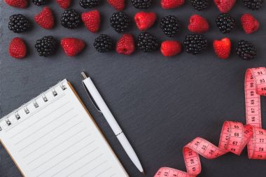 Kırmızı Ahududu, mezura, defter ve bir kalem siyah arduvaz taş zemin üzerine