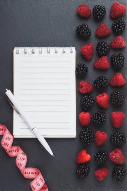 Kırmızı Ahududu, mezura, defter ve bir kalem siyah arduvaz taş zemin üzerine