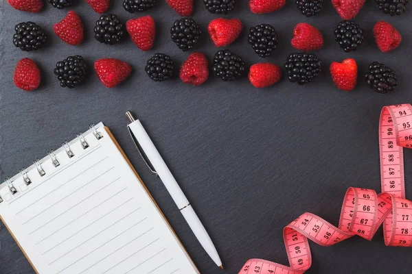 Kırmızı Ahududu, mezura, defter ve bir kalem siyah arduvaz taş zemin üzerine