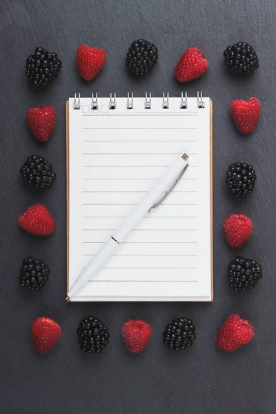 Kırmızı Ahududu, defter ve bir kalem siyah arduvaz taş zemin üzerine