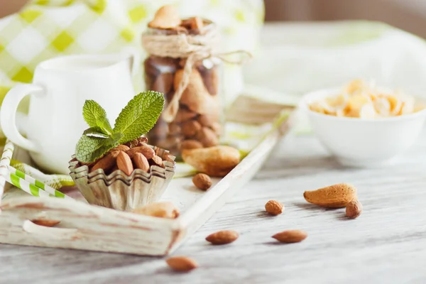 Miel en el tazón, muesli, hojas de menta, almendras y tarro con leche en la bandeja de madera — Foto de Stock