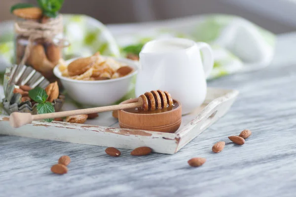 Honey in the bowl, muesli, mint leaves, almonds and jar with milk on the wooden tray — Stock Photo, Image