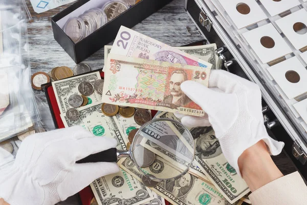 Hands in the white gloves with a magnifying glass and different banknotes — Stock Photo, Image