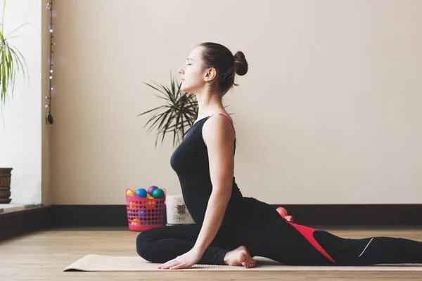 Mujer hace el ejercicio de yoga en la esterilla, en interiores — Foto de Stock