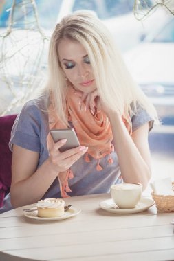 Bir fincan kapuçino ve tatlı plaka üzerinde bir parça ile kafede güzel kadın