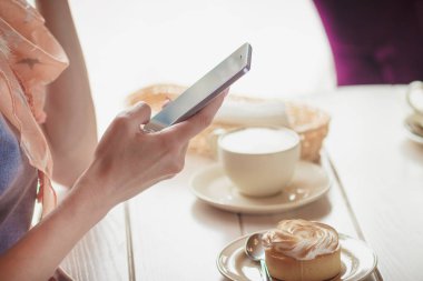 Bir fincan kapuçino ve tatlı plaka üzerinde bir parça ile kafedeki kadına